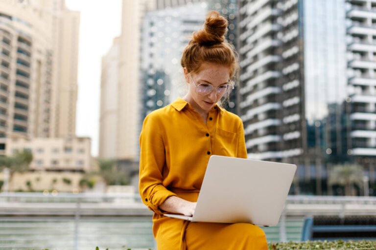 Young Woman sitting in Dubai Marina aria and work on laptop. Student or  freelancer lifestyle.